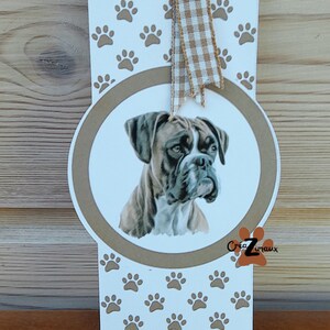 Peut inclure: Signet blanc avec un motif de pattes de chien brun. Un ovale brun avec un dessin d'un boxer est au centre. Le signet a un ruban en vichy brun et blanc attaché au sommet.