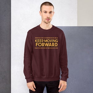 Puede incluir: Una sudadera granate con la frase "KEEP MOVING FORWARD" en letras doradas. La sudadera tambi&eacute;n tiene texto adicional encima y debajo de la frase principal. La persona de la imagen lleva una camisa de color oscuro.