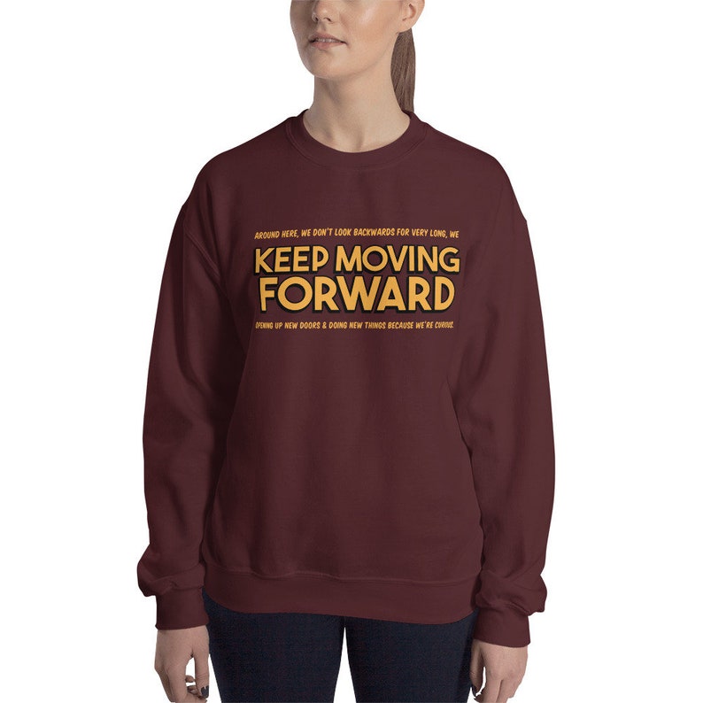 Puede incluir: Una sudadera burdeos con el texto "KEEP MOVING FORWARD" en letras doradas. La sudadera tambi&eacute;n tiene texto adicional encima y debajo de la frase principal. El dise&ntilde;o es sencillo y motivador.