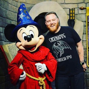 Puede incluir: Mickey Mouse vestido de mago con una t&uacute;nica roja y un sombrero azul con estrellas. Est&aacute; de pie junto a un hombre que lleva una camiseta negra con el texto "Chernabog Fantasia 1940".