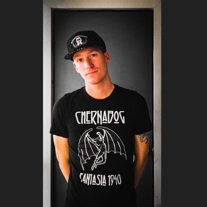 Puede incluir: Una persona con una camiseta negra con un gr&aacute;fico blanco de una figura alada y el texto "Chernadog Fantasia 1940". La persona tambi&eacute;n lleva una gorra de b&eacute;isbol negra con un gr&aacute;fico blanco.