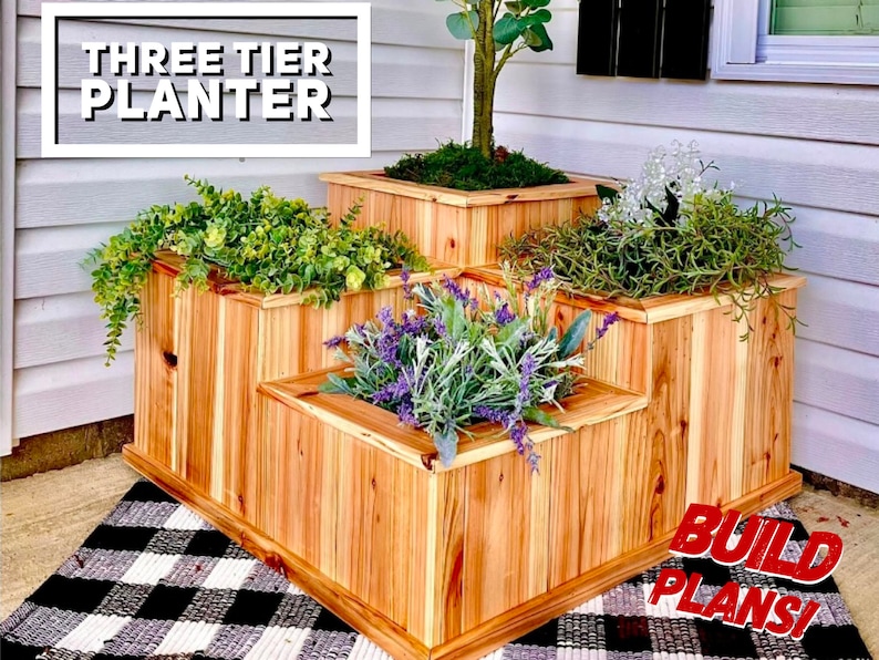 May include: A three-tier wooden planter with three different plants. The planter is made of natural wood and has a rustic look. The text "THREE TIER PLANTER" is displayed at the top of the image. The text "BUILD PLANS!" is displayed at the bottom of the image.