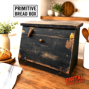 May include: A black wooden bread box with a distressed finish revealing natural wood tones underneath. The box features a slanted front panel, a small wooden knob, and two metal hinges at the base. Text on the image reads PRIMITIVE BREAD BOX.