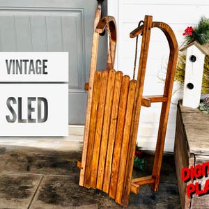 Puede incluir: Trineo de madera vintage con acabado de tinte marrón. El trineo está hecho de listones de madera y tiene una cuerda atada al frente. El trineo está sentado en un porche de madera con una puerta blanca en el fondo. El texto "Vintage Sled" y "Digital Plans" es visible en la imagen.