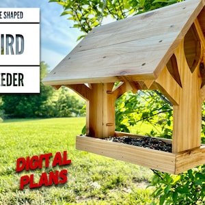 May include: A wooden bird feeder shaped like a tree with a roof. The feeder is filled with birdseed and is hanging from a tree branch. The text "TREE SHAPED BIRD FEEDER DIGITAL PLANS" is visible in the image.
