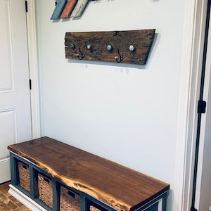 May include: A wooden bench with a live edge walnut top and a dark blue base. The bench has four woven baskets underneath and is in a hallway with a wooden arrow and a rustic wooden coat rack on the wall.