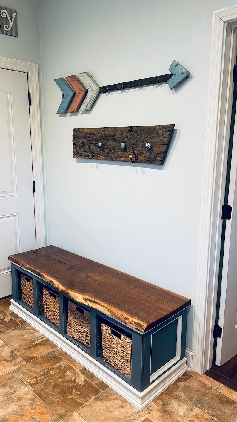 May include: A wooden bench with a live edge walnut top and a dark blue base. The bench has four woven baskets underneath and is in a hallway with a wooden arrow and a rustic wooden coat rack on the wall.
