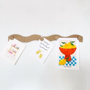May include: A wooden wave-shaped card holder with three cards attached. The cards feature illustrations of a bar cart, a toast, and a bowl of lemons. The text on the cards reads "It's about to get real", "Happy Birthday! Cheers!" and "Les Citrons".