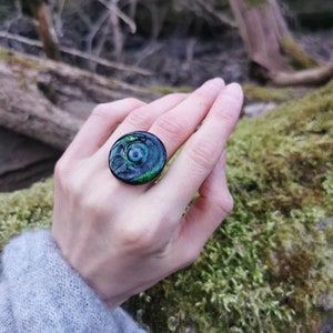 以下が含まれることがあります： 渦巻き模様の濃い緑と黒のリング。リングはガラス製で光沢のある仕上げです。