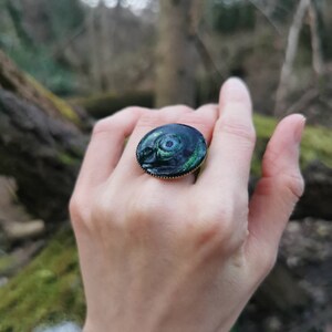 以下が含まれることがあります： 緑と黒のデザインが施された黒い指輪。指輪は丸く、金色のバンドが付いています。