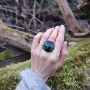 以下が含まれることがあります： 渦巻き模様の黒と緑の指輪。指輪は人の指にはめられています。