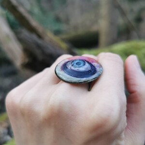 May include: A ring with a large, round, eye-shaped design. The eye is black with a white center and a blue iris. The ring is made of glass and has a silver band.