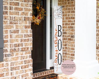 May include: A vertical Halloween-themed wooden sign with the word "BOO" in large black letters. The sign also features the words "Hey There" in orange script, along with spiderweb and swirl designs. The sign is white with vertical stripes.