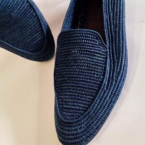 May include: A pair of dark blue woven loafers. The loafers are made of a woven material and have a pointed toe.