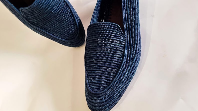 May include: A pair of dark blue woven loafers. The loafers are made of a woven material and have a pointed toe.