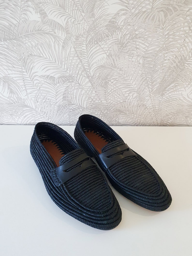 Puede incluir: Un par de mocasines de cuero negro tejido con un dise&ntilde;o trenzado. Los mocasines tienen una punta puntiaguda y una tira de cuero en la parte superior.