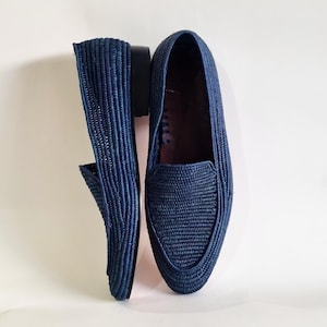 May include: A pair of dark blue woven leather loafers. The loafers have a pointed toe and a flat sole.