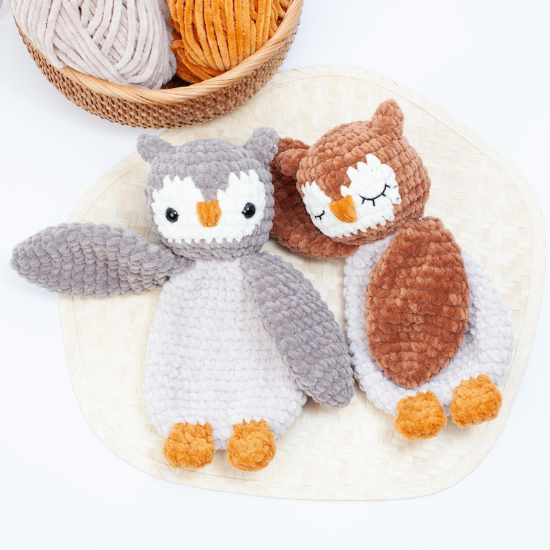 Pu&ograve; includere: Due peluche di gufo all'uncinetto, uno marrone e uno grigio, con occhi e becchi ricamati. I gufi sono sdraiati su un tappetino intrecciato.