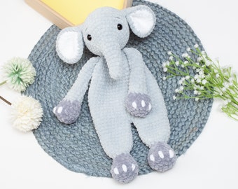 May include: A grey crocheted elephant toy with white accents on the ears and feet. The toy is lying on a grey crocheted mat.