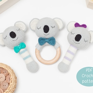 Puede incluir: Tres juguetes de sonajero de koala tejidos a crochet con anillos de madera. El koala de la izquierda tiene una pajarita turquesa, el koala del medio tiene una pajarita turquesa y el koala de la derecha tiene una pajarita morada.  Patrón de crochet PDF.