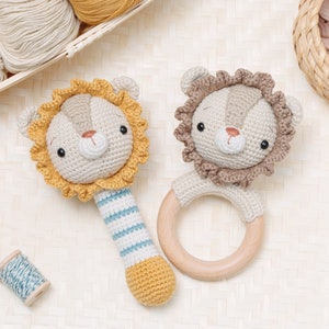 Op de afbeelding: Twee gehaakte leeuwen speelgoedjes. Eén is een rammelaar met een houten ring en de andere is een rammelaar met een gestreepte handvat.