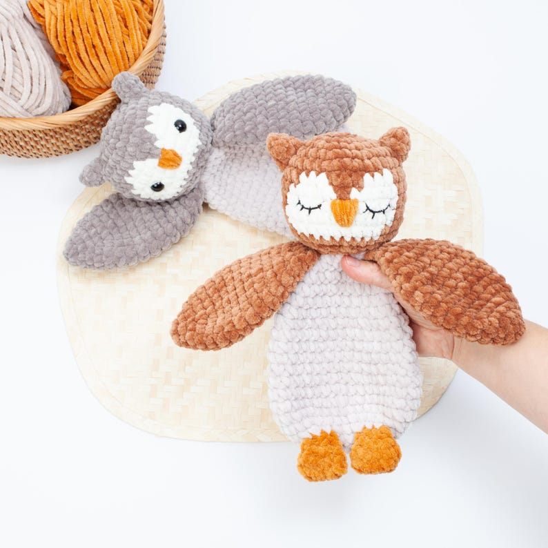 Pu&ograve; includere: Due peluche di gufo all'uncinetto, uno marrone e uno grigio, con gli occhi chiusi e becchi arancioni. Il gufo marrone &egrave; tenuto da una mano.