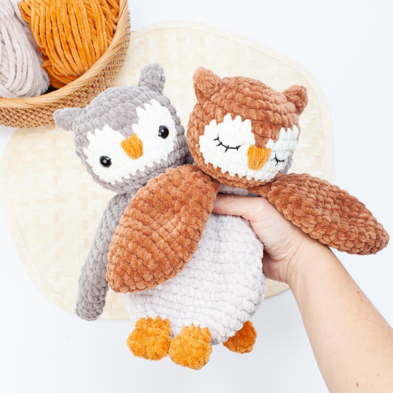 Pu&ograve; includere: Due peluche di gufo all'uncinetto, uno grigio con ali marroni e uno marrone con occhi bianchi e un becco bianco. I gufi sono tenuti in una mano.