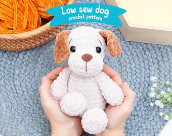 May include: A crocheted white dog with brown ears, sitting in a person's hands. The dog has a brown nose and black eyes. The background is a blue crocheted surface. The text "Low sew dog crochet pattern" is visible in the image.