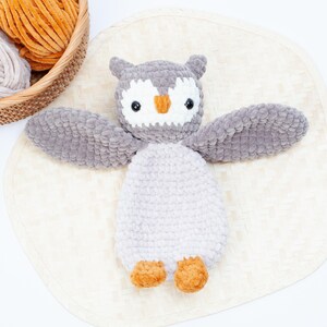 Pu&ograve; includere: Un giocattolo di peluche a forma di gufo grigio lavorato a uncinetto con piedi arancioni. Il gufo ha un viso bianco con occhi neri e un becco arancione.
