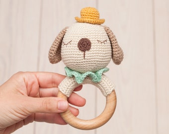 Op de afbeelding: Een gehaakt hondje rammelaar met een houten ring, met een gele hoed en een groene kraag.