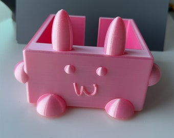 May include: A pink plastic bunny-shaped organizer with a smiling face and rounded feet.