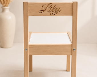 以下が含まれることがあります： 白い座面を持つ正方形の座面と、筆記体で「Lily」という名前が刻印された背もたれを備えた明るい色の木製チェア。4本のまっすぐな脚があり、座面とフレームを接続する金属製の金具が見える。
