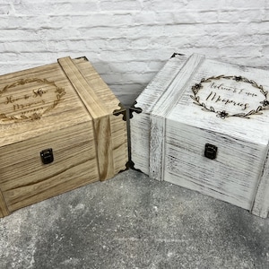 May include: Two wooden keepsake boxes, one light brown and one white, with decorative metal corner brackets and clasps. The light brown box has the text "Her & His Memories" in a floral wreath. The white box has the text "Adriana & Emma Memories" in a floral wreath.