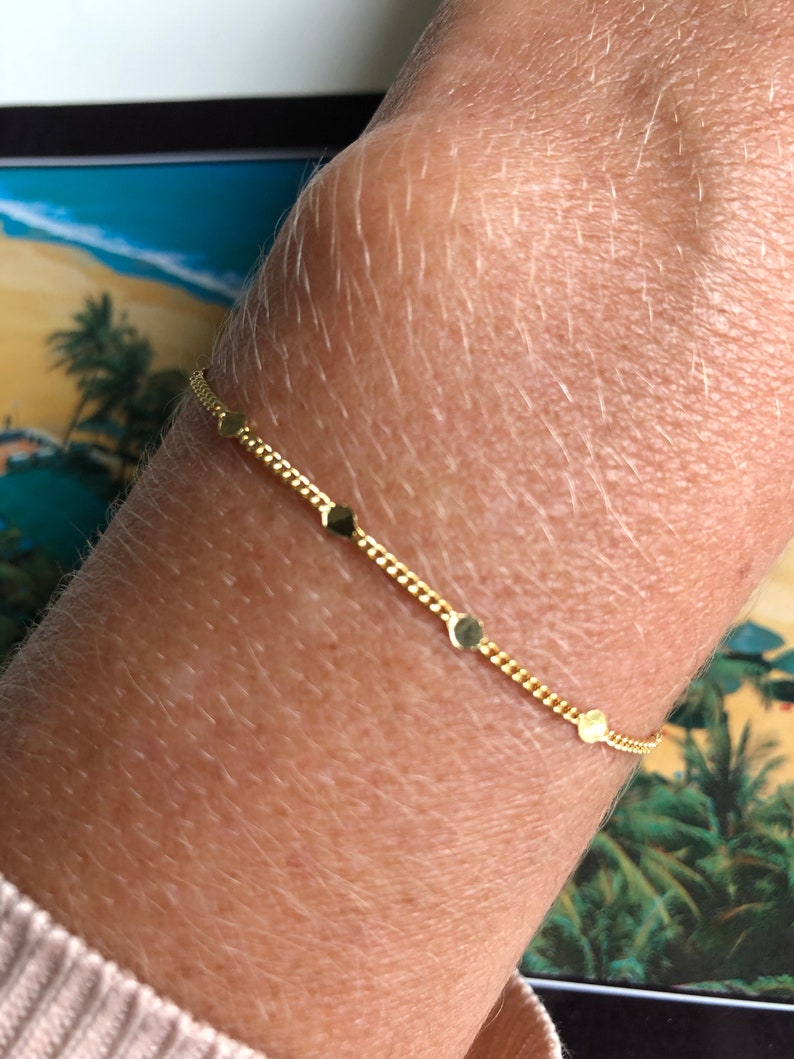 Puede incluir: Una delicada pulsera dorada con peque&ntilde;os abalorios redondos y un dise&ntilde;o de cadena. La pulsera se lleva en la mu&ntilde;eca, mostrando su simple elegancia. La pulsera mide aproximadamente 17,78 cm de largo.