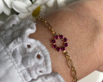 Puede incluir: Un brazalete de cadena dorada con un dije de flor de pedrería rosa.