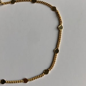 Puede incluir: Un collar de cadena de color dorado con peque&ntilde;os dijes redondos y planos espaciados uniformemente a lo largo de la cadena. El collar tiene una apariencia delicada y se destaca sobre un fondo blanco. La cadena es de estilo cl&aacute;sico de eslabones y los dijes a&ntilde;aden un toque de elegancia.
