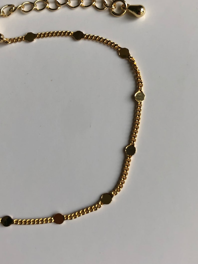 Puede incluir: Un collar de cadena de color dorado con peque&ntilde;os dijes redondos y planos espaciados uniformemente a lo largo de la cadena. El collar tiene una apariencia delicada y se destaca sobre un fondo blanco. La cadena es de estilo cl&aacute;sico de eslabones y los dijes a&ntilde;aden un toque de elegancia.