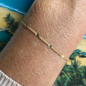 Puede incluir: Una delicada pulsera dorada con una cadena y peque&ntilde;os dijes planos en forma de coraz&oacute;n. La pulsera se lleva en la mu&ntilde;eca, mostrando su elegancia sencilla. El color dorado proporciona un c&aacute;lido contraste con la piel.