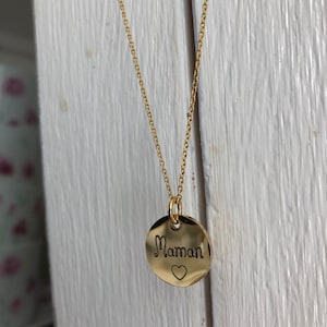 May include: A gold necklace with a round pendant that says "Maman" with a small heart below the word.