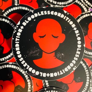 May include: A black and white sticker with the text "Bloodless Condition + Bloodless Condition" in a circle around a red silhouette of a person with closed eyes. The text is in a distressed font.
