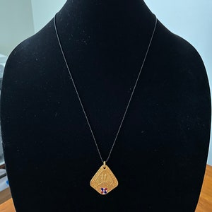 May include: A gold-toned pendant necklace with a square-shaped pendant featuring a design of two figures holding hands. The pendant has a red, white, and blue enamel inlay in the center.