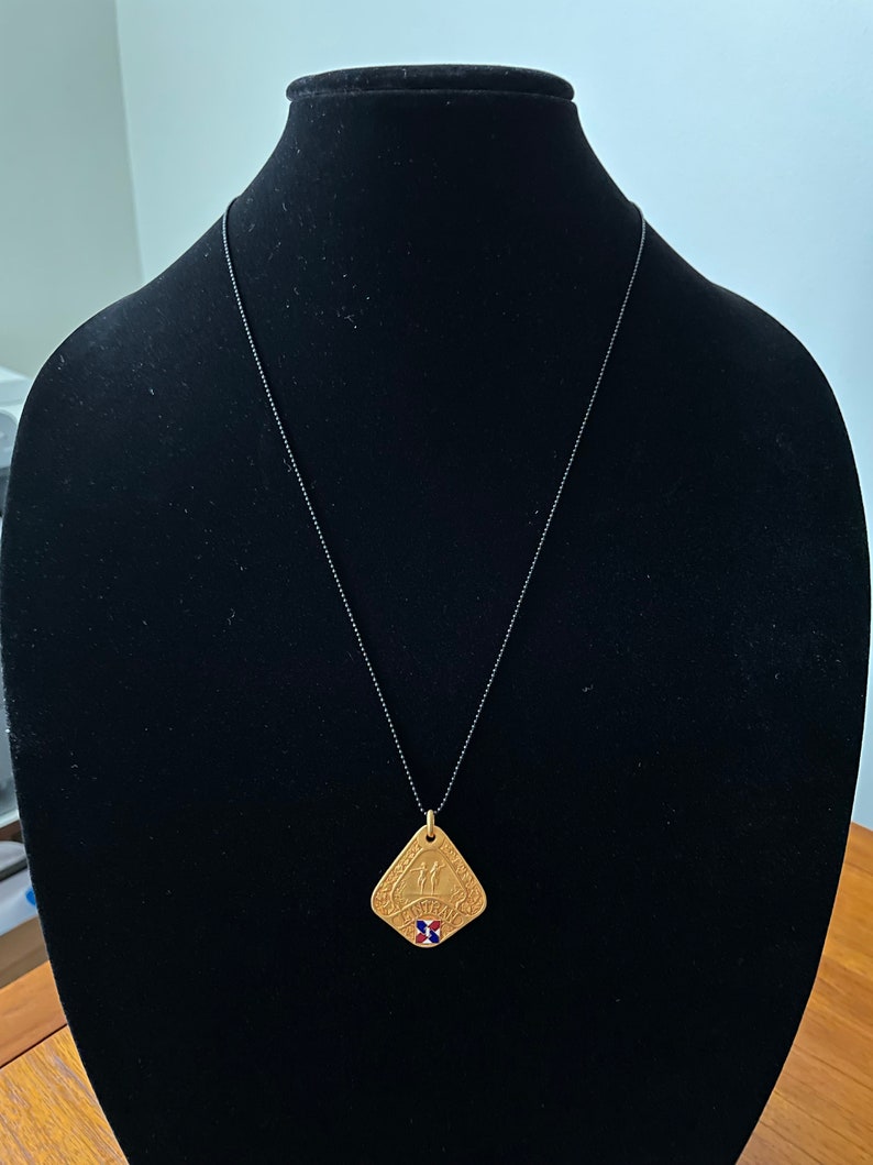 May include: A gold-toned pendant necklace with a square-shaped pendant featuring a design of two figures holding hands. The pendant has a red, white, and blue enamel inlay in the center.
