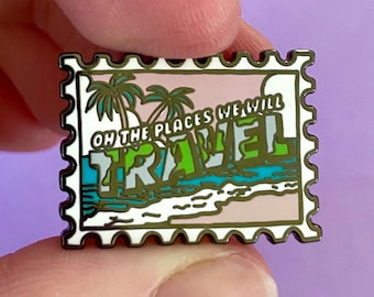 May include: A gold-colored enamel pin shaped like a vintage postcard with the text "Oh the places we will travel" and a beach scene with palm trees.