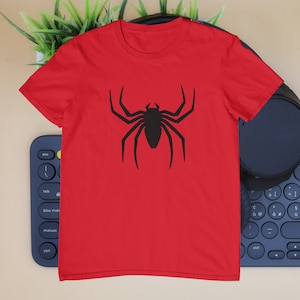 Puede incluir: Una camiseta roja de manga corta con un gr&aacute;fico negro grande y centrado de una ara&ntilde;a con ocho patas largas y puntiagudas y un cuerpo segmentado. La prenda tiene un cuello redondo cl&aacute;sico y est&aacute; confeccionada con un tejido liso y uniforme.