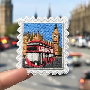 May include: A square embroidered patch shaped like a postage stamp featuring a red double-decker bus with the word LONDON printed on the front, set against a background of the Elizabeth Tower and the Houses of Parliament under a blue sky.