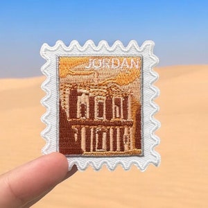 Op de afbeelding: Een witte geborduurde patch met een bruine afbeelding van het schatkistgebouw in Petra, Jordanië. De patch heeft een witte rand met een gegolfde rand en het woord "JORDANIË" in wit bovenaan gedrukt.