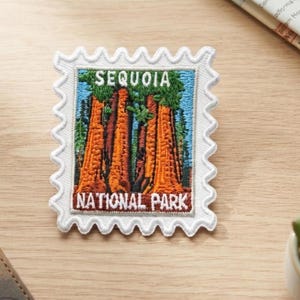 Può includere: Una toppa ricamata rettangolare a forma di francobollo con un bordo bianco smerlato. Il disegno raffigura sequoie arancioni su un cielo blu, con la scritta "SEQUOIA" in alto e "NATIONAL PARK" nella parte inferiore della toppa.