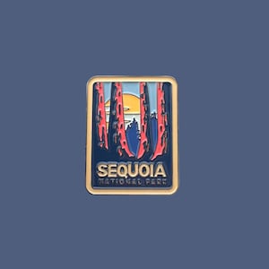 Könnte beinhalten: Goldfarbener Pin mit blauem Hintergrund und einer roten und orangen Sonnenuntergangsszene. Der Text "SEQUOIA NATIONAL PARK" ist in Weiß auf einem schwarzen Banner gedruckt.