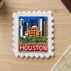 Può includere: Una toppa ricamata rettangolare a forma di francobollo con un bordo bianco smerlato. Il design presenta lo skyline della città di Houston con edifici alti, alberi verdi e la parola HOUSTON in lettere rosse su uno stendardo.