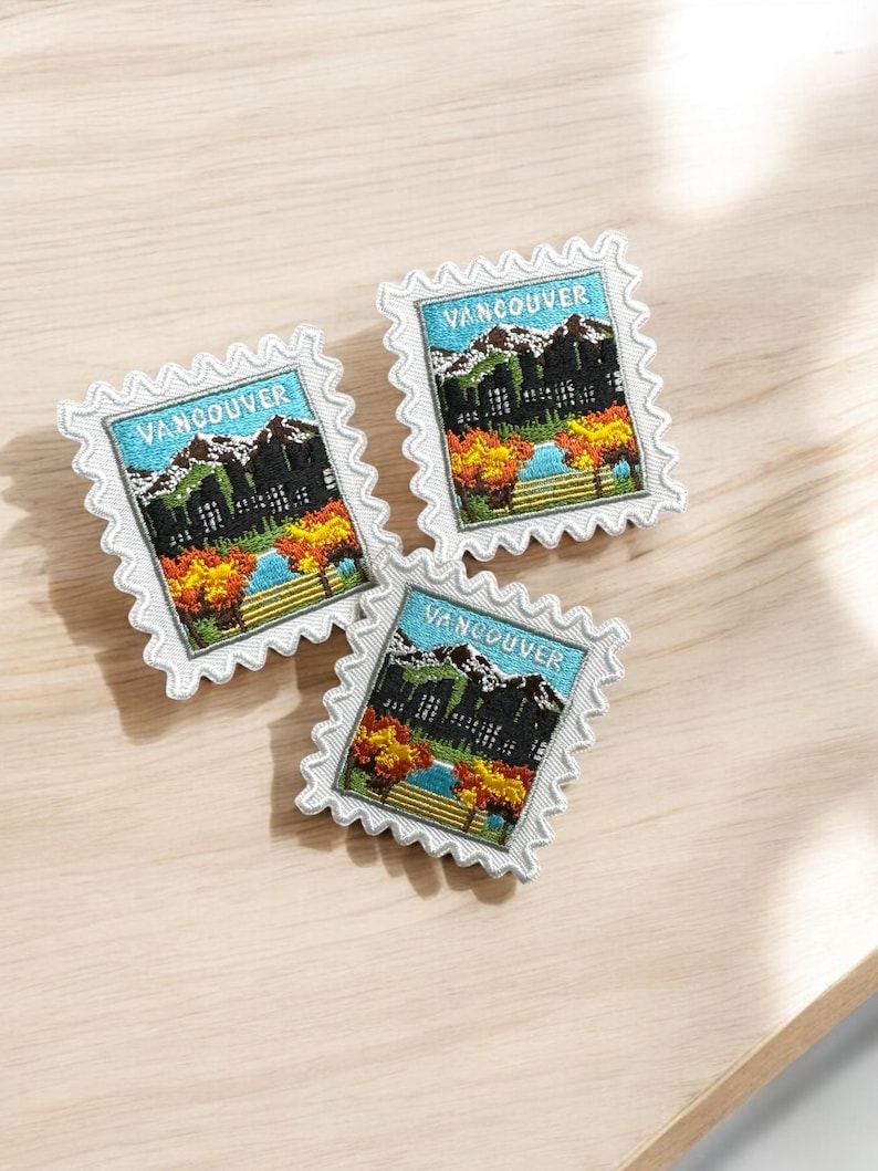 Puede incluir: Tres parches bordados rectangulares con forma de sello postal y bordes blancos festoneados. Cada parche muestra un paisaje de Vancouver con monta&ntilde;as nevadas, cielo azul, una masa de agua y &aacute;rboles de oto&ntilde;o en tonos naranja y amarillo.